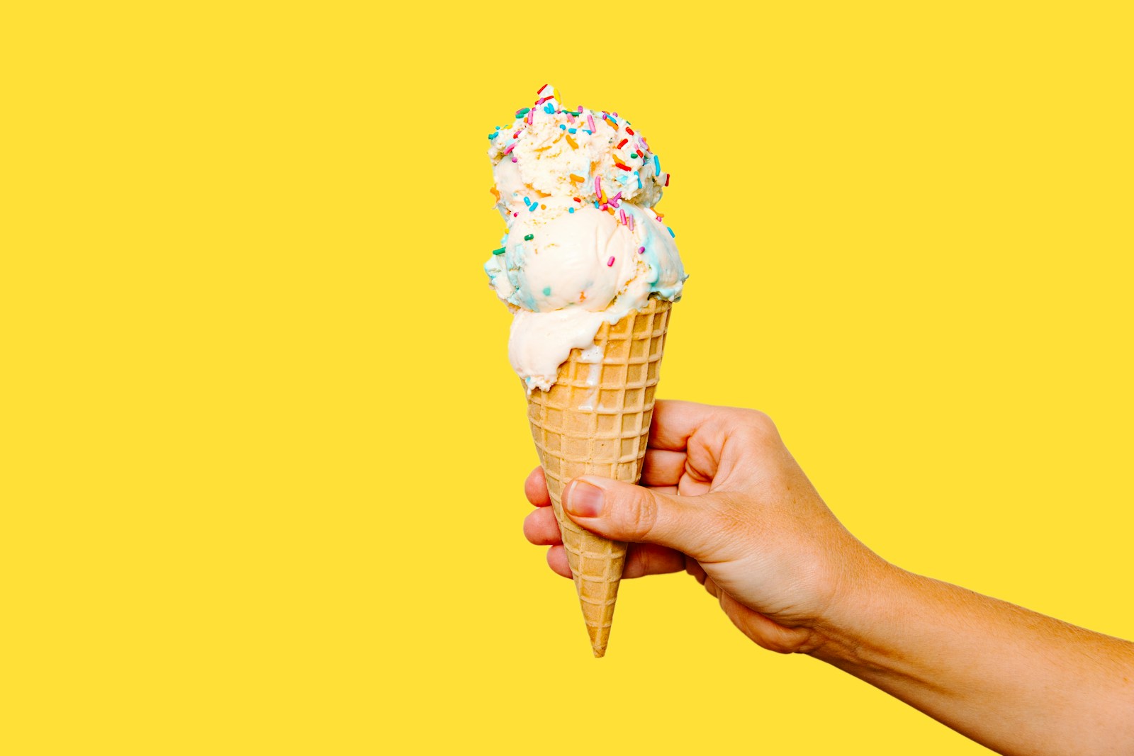 Hand hält eine Eiswaffel mit Streuseln – Symbolbild für Eisdielen und Eiscafés