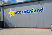 Grauer Hallenbau mit dem Sternenland-Schriftzug und Parkplatz davor