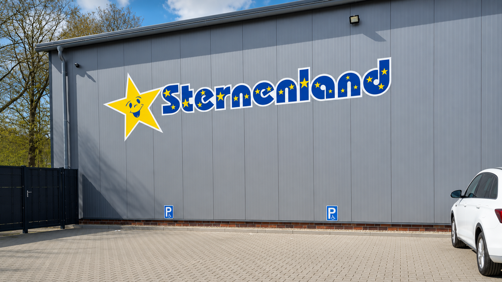 Grauer Hallenbau mit dem Sternenland-Schriftzug und Parkplatz davor