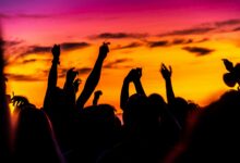 Publikum mit erhobenen Händen als Silhouetten vor Abendhimmel bei einem Open-Air-Konzert – Symbolbild