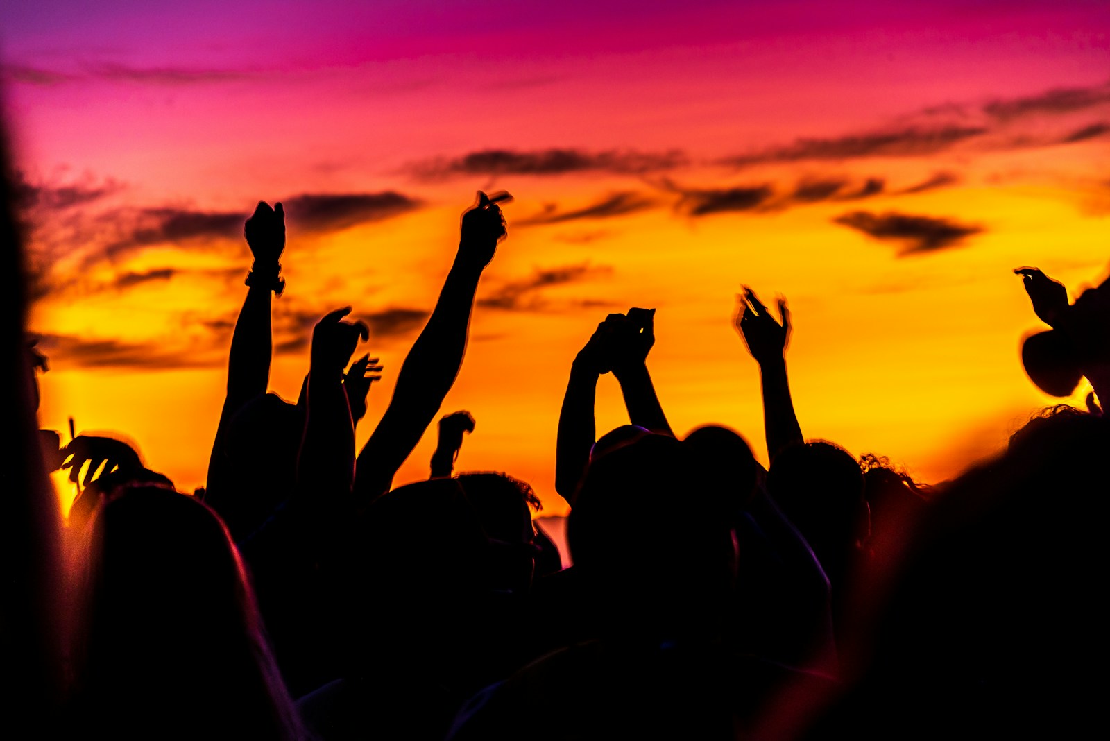 Publikum mit erhobenen Händen als Silhouetten vor Abendhimmel bei einem Open-Air-Konzert – Symbolbild