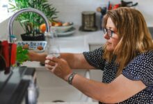 Eine Frau füllt ein Glas mit Wasser am Wasserhahn