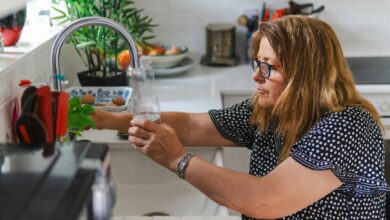 Eine Frau füllt ein Glas mit Wasser am Wasserhahn