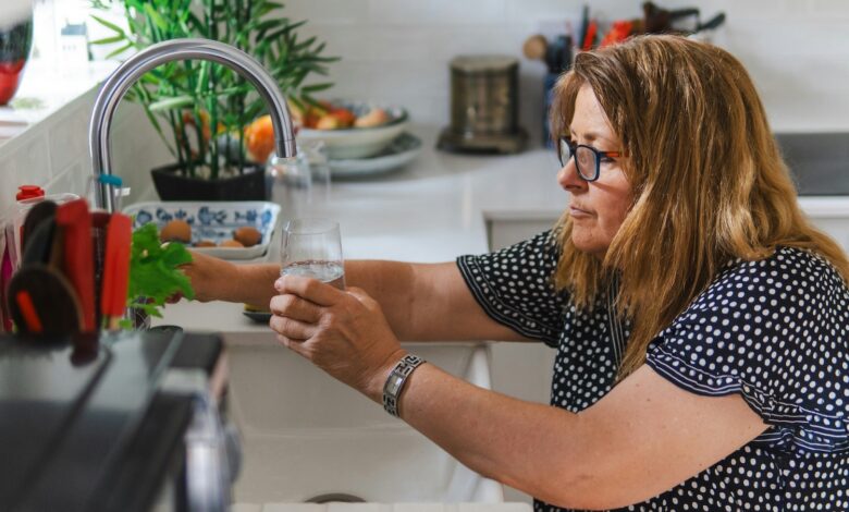 Eine Frau füllt ein Glas mit Wasser am Wasserhahn
