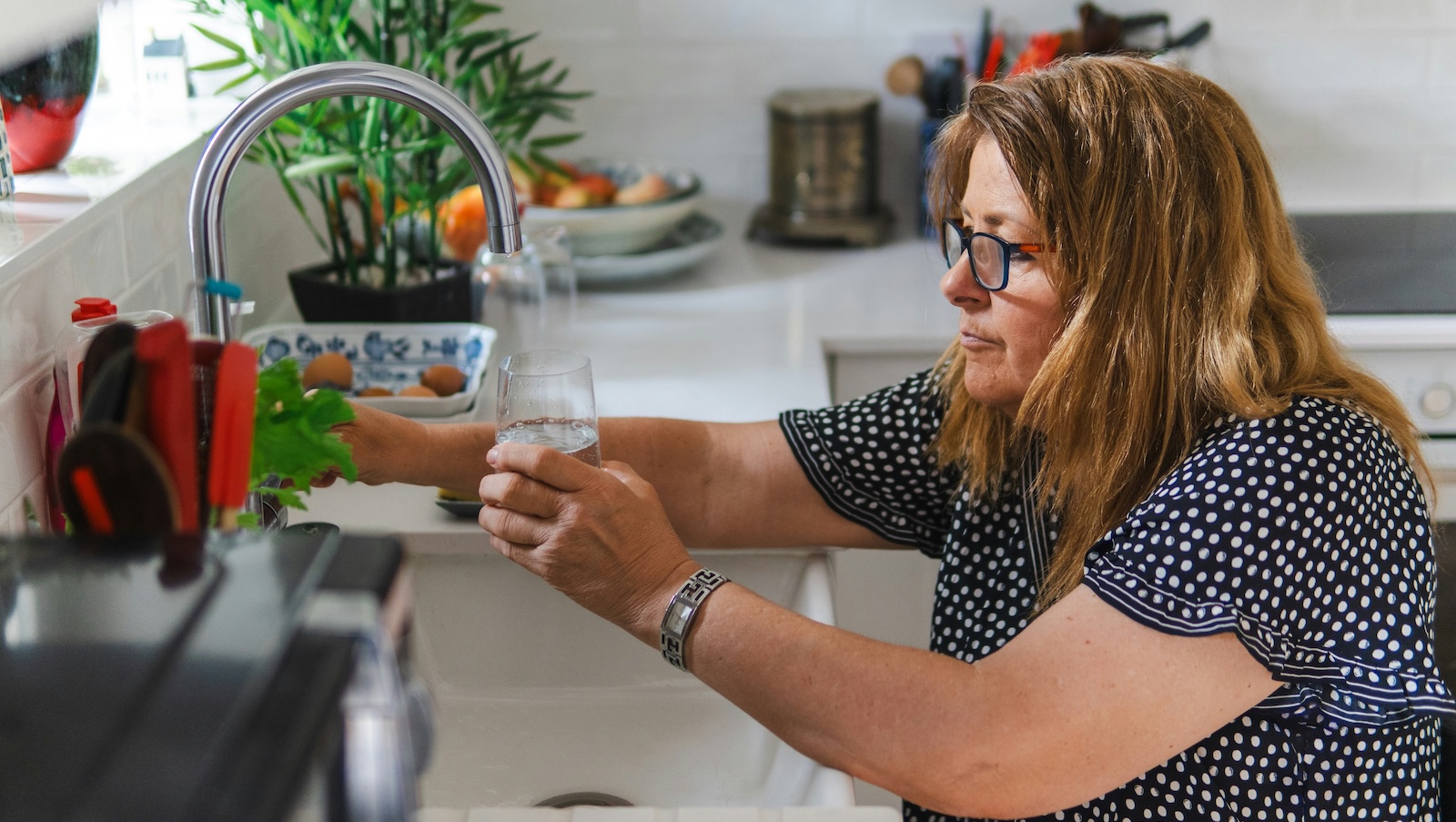Eine Frau füllt ein Glas mit Wasser am Wasserhahn