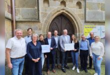 Gruppenfoto mit Nikolaus Jansen, Bürgermeister Norbert Hüsing, Samtgemeindebürgermeister Matthias Sils und weiteren Beteiligten vor der Katholischen Kirche St. Vitus in Lünne