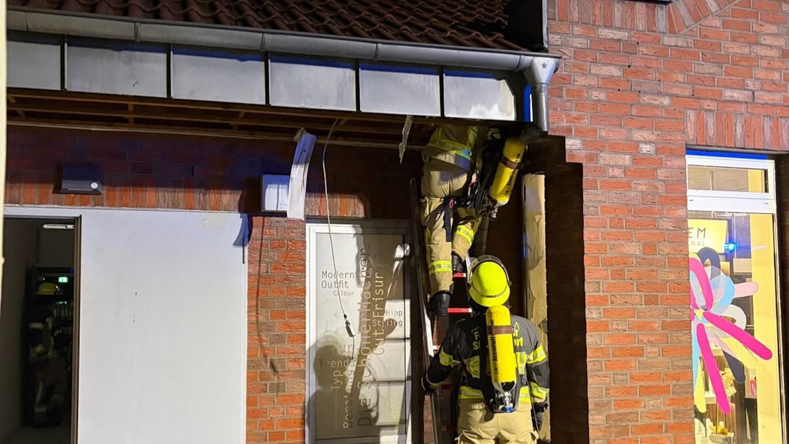 Feuerwehrleute mit Atemschutz auf einer Steigleiter bei der Kontrolle des Gebäudes am Verbrauchermarkt in Schüttorf