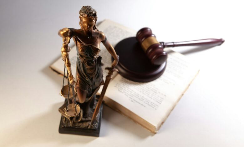 Statue der Justitia mit Waage neben Gesetzbüchern, Symbolbild Justiz