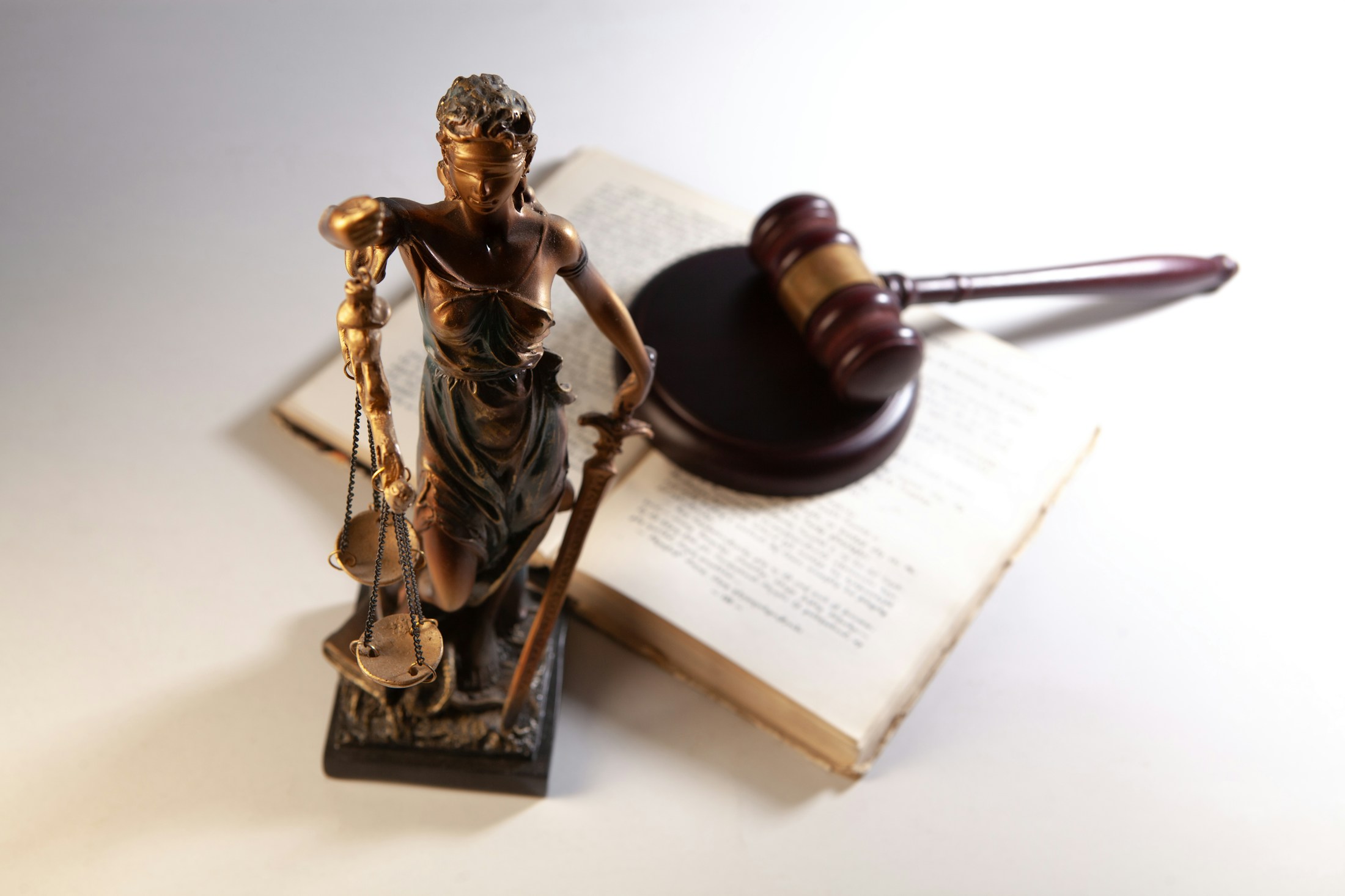 Statue der Justitia mit Waage neben Gesetzbüchern, Symbolbild Justiz