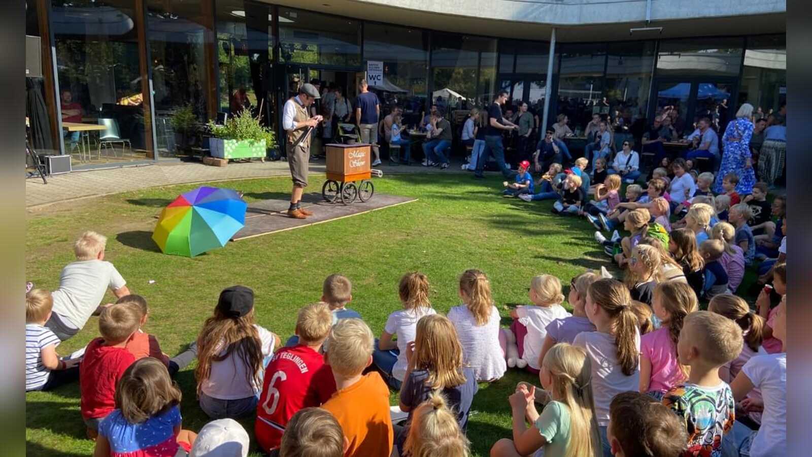 Kinder sitzen im Kreis um eine Bühne beim Kindertag in Meppen