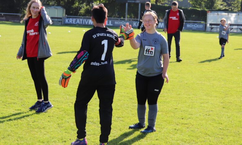 Mannschaften und Zuschauer stehen sich auf dem Sportplatz gegenüber, Spieler heben die Hand