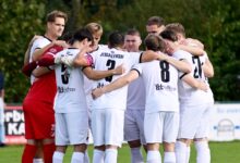 Spieler des SC Spelle-Venhaus in weißen Trikots stehen beim Derby in Hemsen im Kreis zusammen