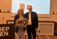 Dr. Sigrid Kraujuttis mit Blumenstrauß neben einem Gratulanten im Ratssaal Meppen, im Hintergrund die Präsentation der Wahlergebnisse