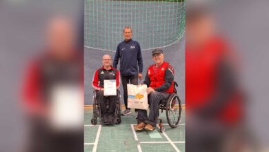 Thomas Hilmes mit Urkunde und Geschenktasche im Rollstuhl, daneben Willi Fenslage und Günter Hömmeke in der Sporthalle