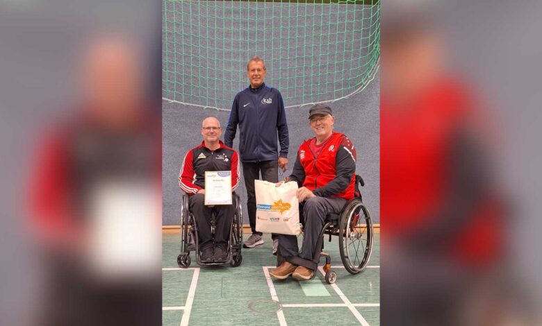 Thomas Hilmes mit Urkunde und Geschenktasche im Rollstuhl, daneben Willi Fenslage und Günter Hömmeke in der Sporthalle