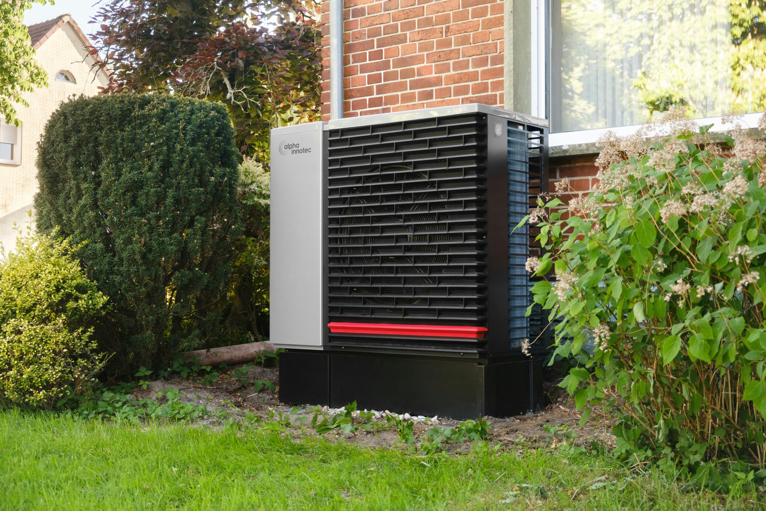 Moderne Wärmepumpe vor einem sanierten Wohnhaus