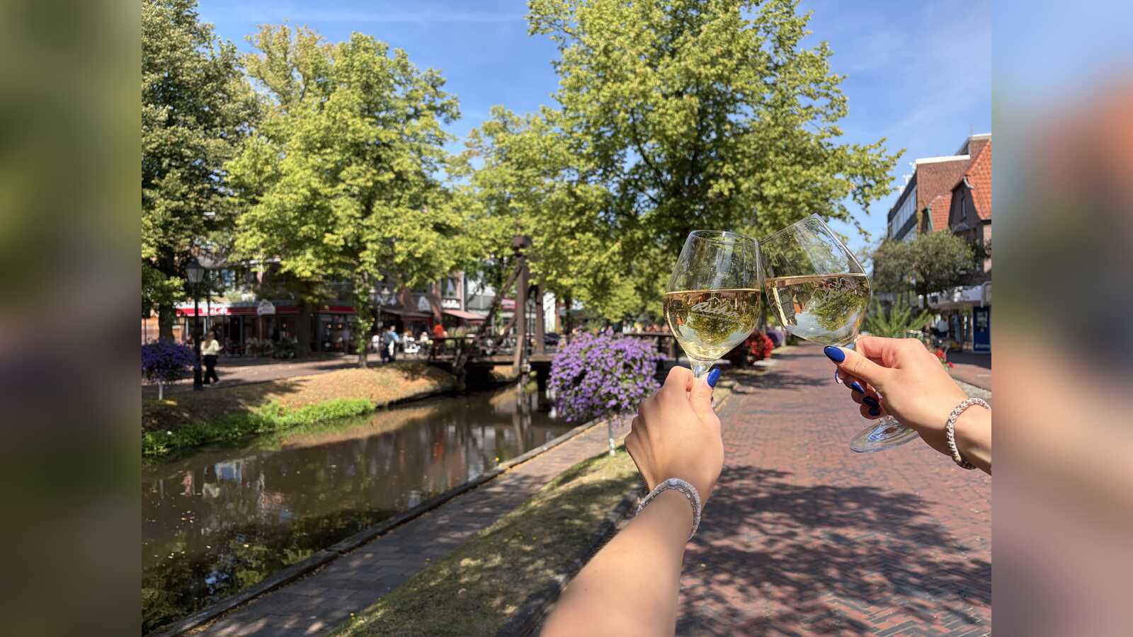 Zwei Hände stoßen mit Weingläsern am Hauptkanal in Papenburg an