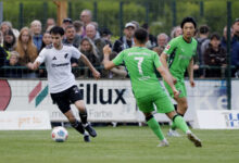 Anton Popov vom SC Spelle-Venhaus im weißen Trikot am Ball, zwei Gegenspieler in Grün laufen auf ihn zu