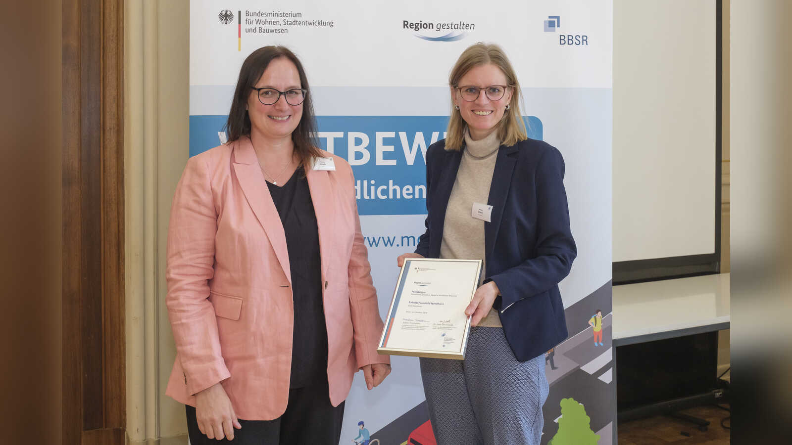 Melanie Schade vom BBSR überreicht Nordhorns Stadtbaurätin Milena Schauer die Siegerurkunde