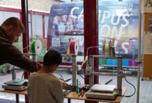 Ein Junge arbeitet mit einem Betreuer an 3D-Druckern, im Hintergrund der Transporter Campus on Wheels