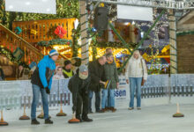 Gruppe beim Eisstockschießen auf der Eisbahn vor den beleuchteten Buden des Lingener Weihnachtsmarktes