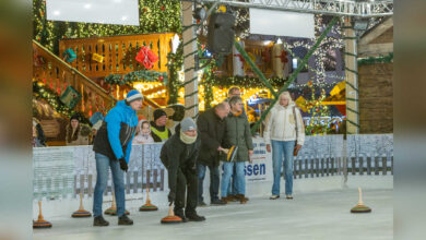 Gruppe beim Eisstockschießen auf der Eisbahn vor den beleuchteten Buden des Lingener Weihnachtsmarktes