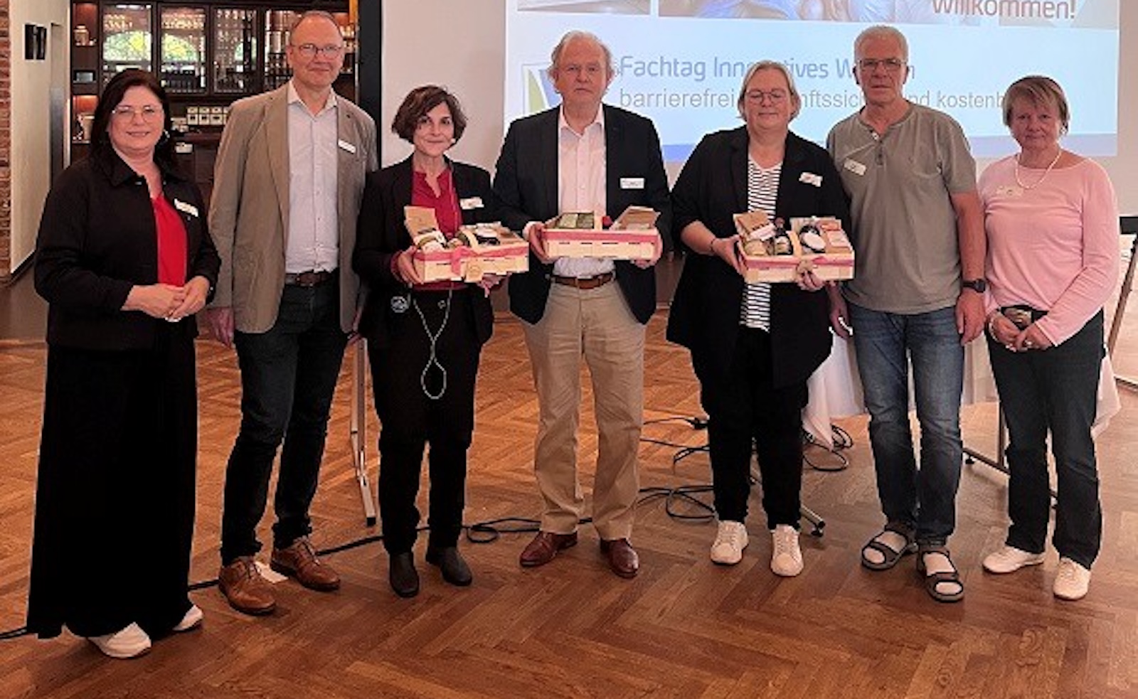 Sieben Personen stehen vor einer Leinwand mit dem Titel des Fachtags Innovatives Wohnen