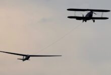 Doppeldecker im Flugzeugschlepp mit einem Segelflugzeug am Seil vor grauem Abendhimmel