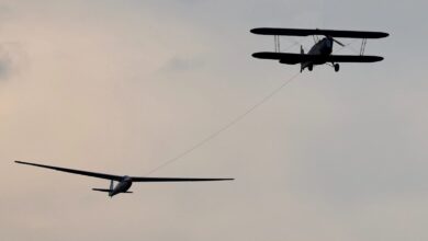 Doppeldecker im Flugzeugschlepp mit einem Segelflugzeug am Seil vor grauem Abendhimmel