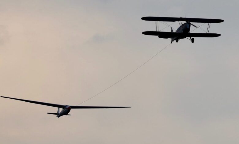 Doppeldecker im Flugzeugschlepp mit einem Segelflugzeug am Seil vor grauem Abendhimmel