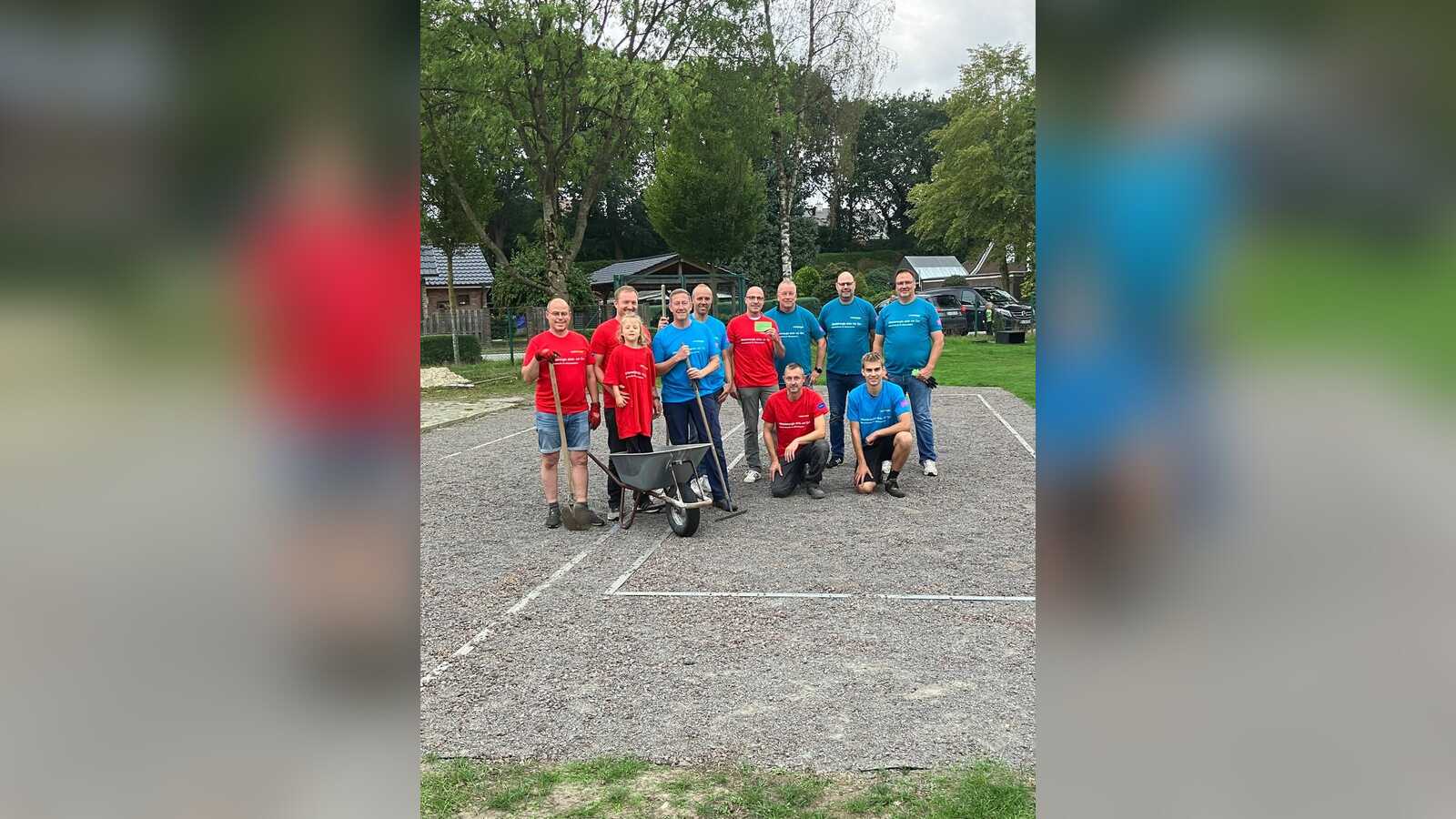 Gruppe von Helfern mit Schubkarre und Rechen auf der fertigen Bouleplatzfläche