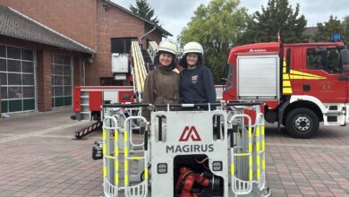 Zwei junge Frauen mit Feuerwehrhelmen stehen hinter dem Rettungskorb einer Drehleiter vor der Feuerwache Lingen