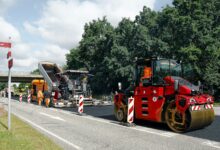 Straßenbaustelle mit roter Walze und Asphaltfertiger beim Einbau einer neuen Asphaltschicht