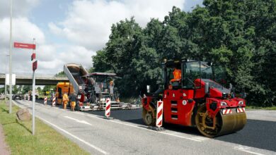 Straßenbaustelle mit roter Walze und Asphaltfertiger beim Einbau einer neuen Asphaltschicht