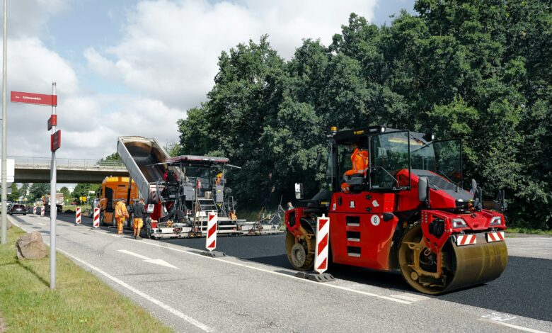 Straßenbaustelle mit roter Walze und Asphaltfertiger beim Einbau einer neuen Asphaltschicht