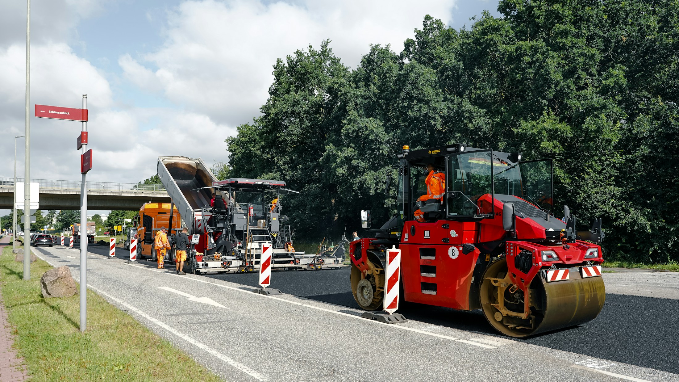 Straßenbaustelle mit roter Walze und Asphaltfertiger beim Einbau einer neuen Asphaltschicht