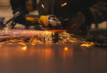 Ein Mann bearbeitet in einer Werkstatt ein Metallteil mit einem Winkelschleifer, Funken sprühen