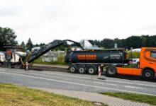 Eine Straßenfräse trägt die alte Asphaltdecke ab und lädt sie auf einen Lkw