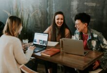Mehrere Menschen sitzen mit Laptops an einem Tisch und tauschen sich aus