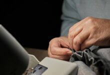 Hände legen grauen Stoff unter den Fuß einer Nähmaschine