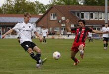 Tjark Höpfner im weißen Trikot des SC Spelle-Venhaus spielt den Ball, ein Gegenspieler in Rot-Schwarz grätscht