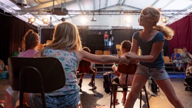 Kinder proben eine Theaterszene mit Stühlen auf einer Bühne mit Scheinwerfern